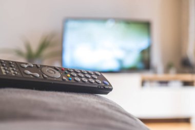 Ön planda TV uzaktan kumandası, bulanık arkaplanda TV. Akıyor.