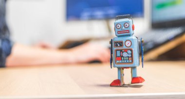 Masaüstünde oyuncak robot, arkada bilgisayarda çalışan adam. Yapay zeka, sohbet robotları veya sosyal robotlar ve algoritmalar için sembol