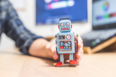 Masaüstünde oyuncak robot, arkada bilgisayarda çalışan adam. Yapay zeka, sohbet robotları veya sosyal robotlar ve algoritmalar için sembol