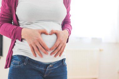 Hamile karnını kapat, anne elleriyle bir kalp oluşturuyor.