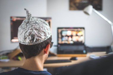 Young man is wearing aluminum cap, conspiracy theory concept clipart