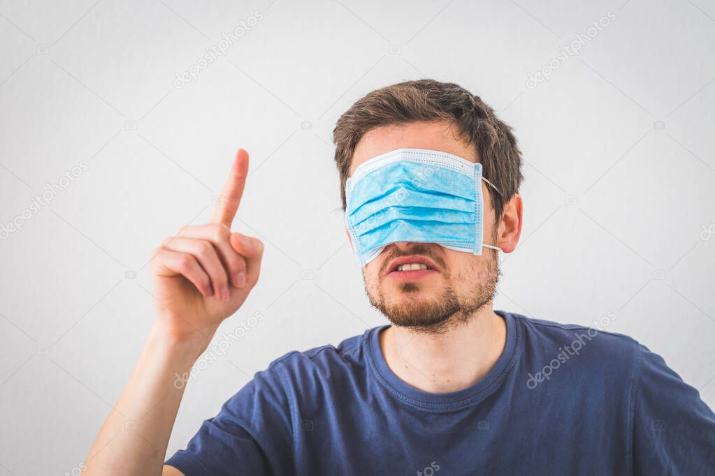 Young angry man with and face mask is gesturing angry. Conspiracy theory concept.