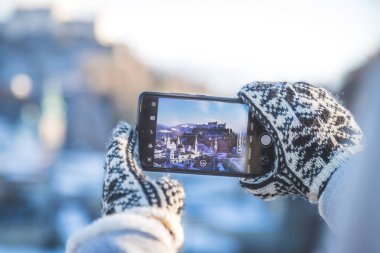 Genç turist kadın, kış zamanı akıllı telefonuyla Salzburg 'un fotoğrafını çekiyor.