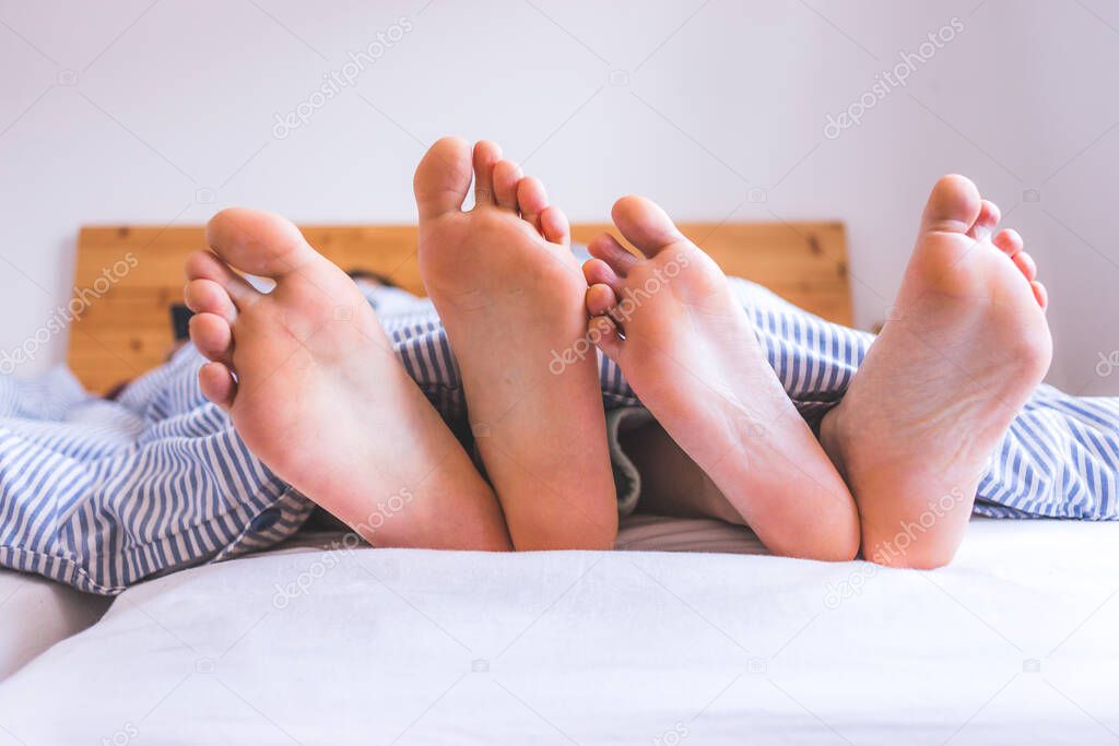 Close up a couples uncovered feet sleeping in bed, morning