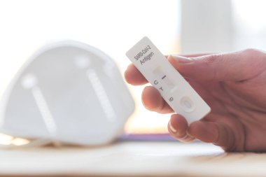 Ekspres antijen covid testi tutan parmakları kapat, negatif sonuç, bulanık arkaplanda ffp2 maskesi