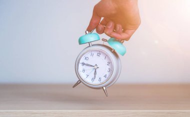 Erkek el, geriye dönük beyaz bir çalar saat tutuyor.