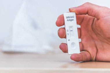 Ekspres antijen covid testi tutan parmakları kapat, negatif sonuç, bulanık arkaplanda ffp2 maskesi