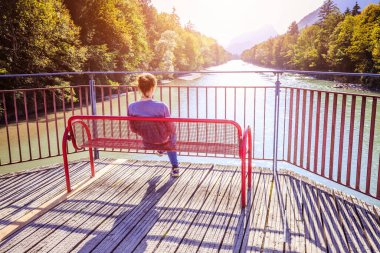 Genç kadın bankta oturuyor, nehir manzarasının tadını çıkarıyor.