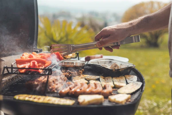 Close up of sausages, steak, cheese and vegetables on gas grill. Summer time, outdoors.