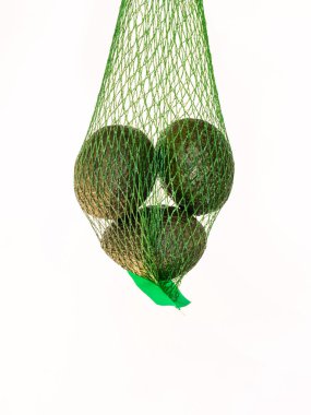 Stüdyonun arka planında beyaz bir arkaplan ile izole edilmiş ve askıya alınmış yeşil bir ağdaki avokadolar