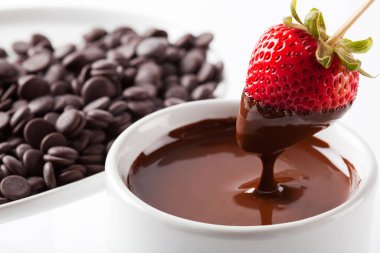 Çilek siyah çikolataya batırılıyor. Stüdyoda izole edilmiş, beyaz arka planda.