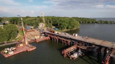 Nehir üzerinde bir köprü inşa edilişinin 4K Top Manzarası. İnşaat işi, yeni bir köprü..