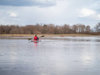 A girl with a dog on a red kayak swims in the distance on the horizon .
