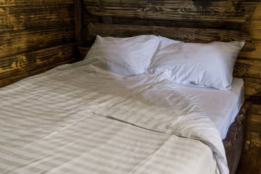 Yatak odasının içi akşam. Döşeği, yastığı ve yorganı olan çift kişilik ahşap bir yatak. Odanın duvarları ahşap panellerle kaplı.