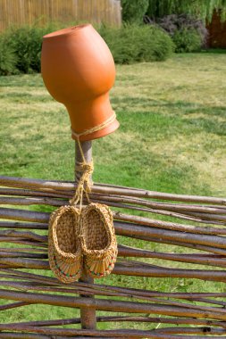 Crock and bast shoes on wicker fence clipart