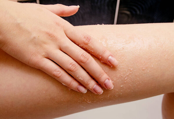 В рамке рука девушки очищает кожу бедра солью для массажа.