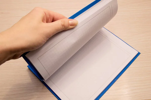 ノートのためのケージ内の白いきれいなノートは木製の背景にあり 女性の左の手はノートブックのシートを通って反転します — ストック写真