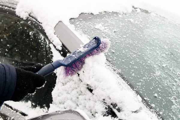 Male driver sweeps snow off car windscreen with special brush