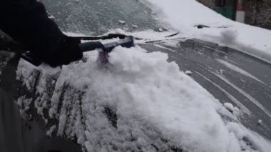 Erkek sürücü karları özel bir fırçayla arabanın ön camından temizliyor.