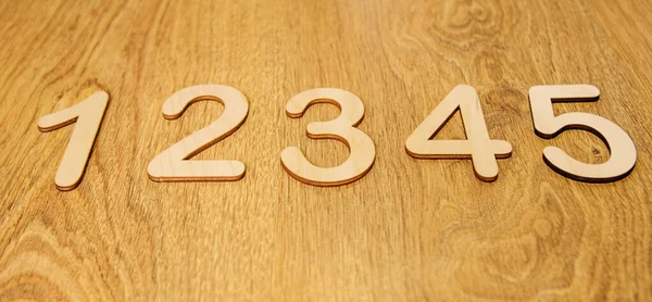 Flatley, side view of large wooden numbers one, two, three, four and five lying in order on a wooden background