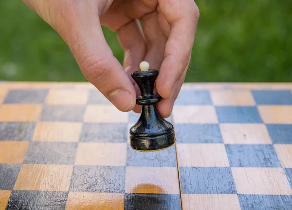Male hand holding one black queen chess piece over an empty chessboard