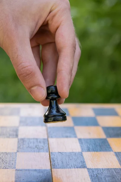 Male hand holding one chess piece of black pawn over empty chessboard