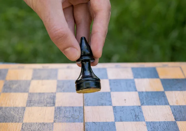 Male hand holding one chess piece of black bishop over empty chessboard