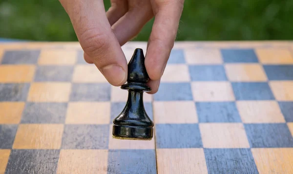 Male hand holding one chess piece of black bishop over empty chessboard