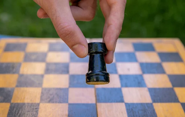 Male hand holding one chess piece of black rook over empty chessboard