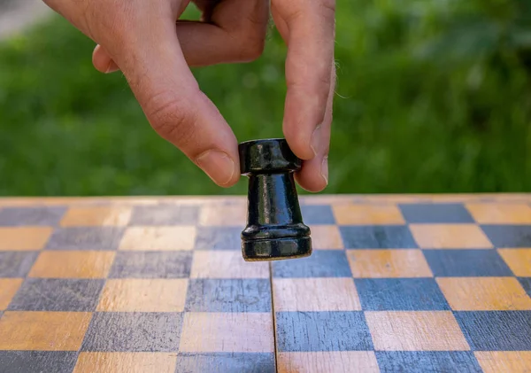 Male hand holding one chess piece of black rook over empty chessboard