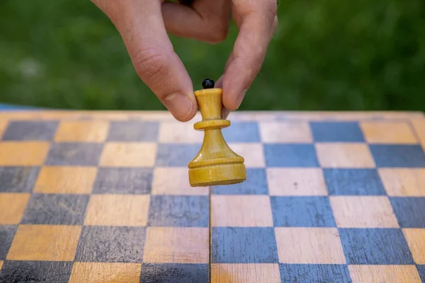 Male hand holding one chess piece of white queen over empty chessboard