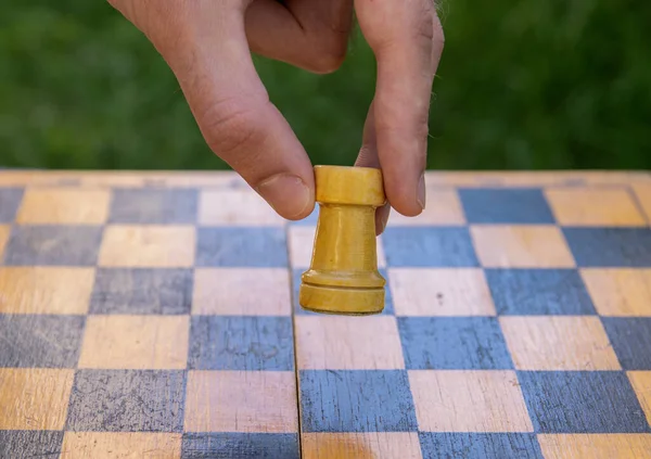 Male hand holding one chess piece of white rook over empty chessboard