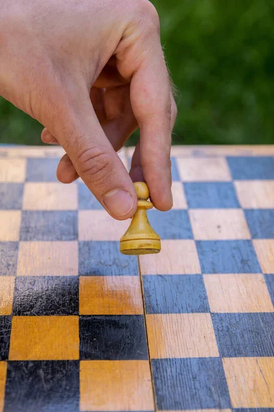 Male hand holding one chess piece of white pawn over empty chessboard