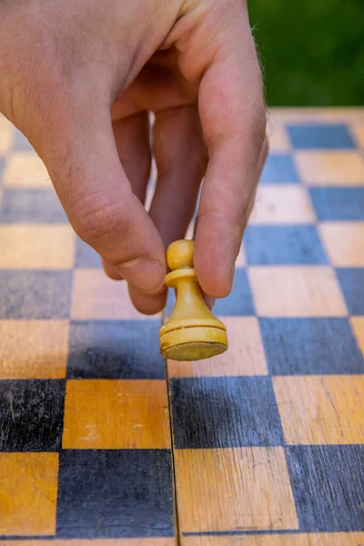 Male hand holding one chess piece of white pawn over empty chessboard