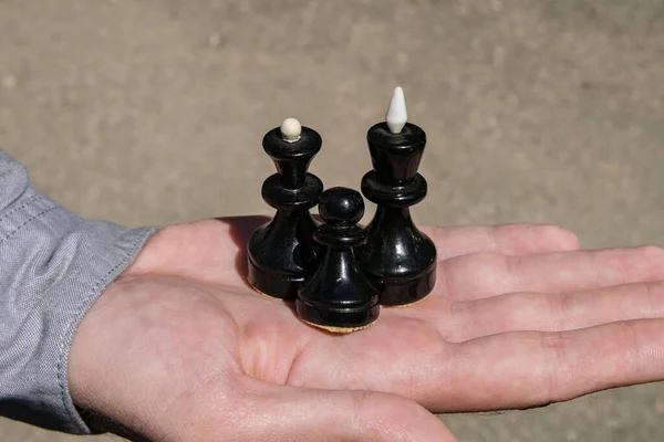 Three black chess pieces: king, queen and pawn on a man\'s palm form an example of a family
