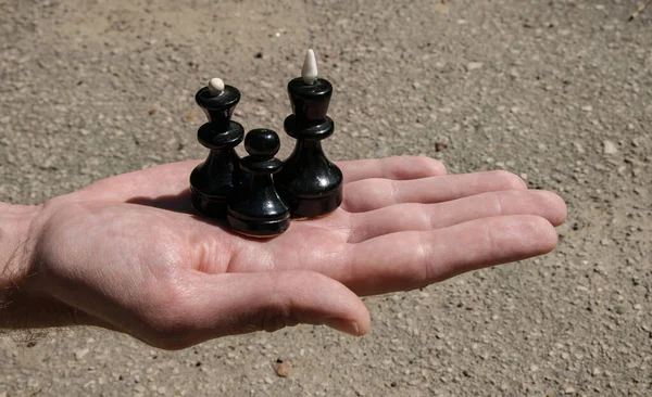 Three black chess pieces: king, queen and pawn on a man's palm form an example of a family