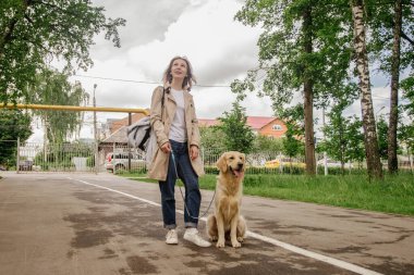 Ev sahibesi kız Golden Retriever köpeğiyle parkta yürüyor.