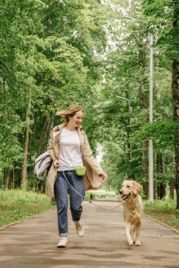 Ev sahibesi kız Golden Retriever köpeğiyle parkta yürüyor.