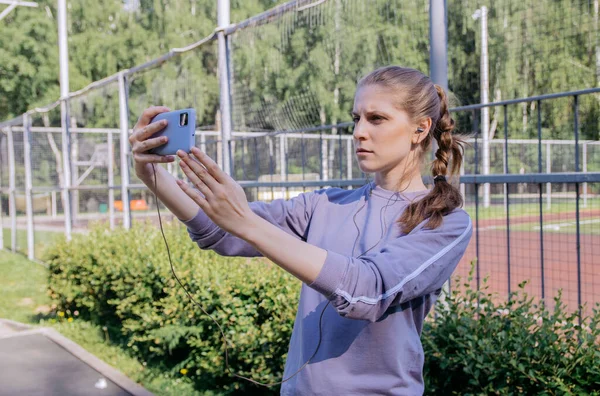Spor Üniformalı Bir Kız Antreman Sitesinde Kulaklıklar Elinde Bir Telefonla — Stok fotoğraf