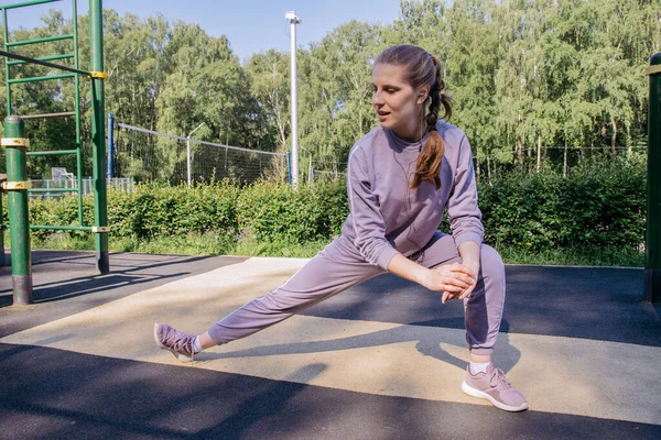 ヘッドフォンの女の子と遊び場のスポーツの制服は足のストレッチを実行します — ストック写真