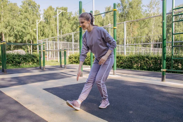 ヘッドフォンの女の子と遊び場のスポーツの制服は 足のストレッチ運動を実行します — ストック写真