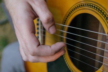 male hand playing guitar strings close up in nature
