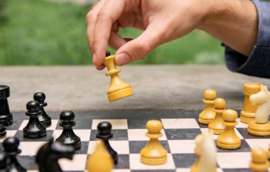 Bir adam beyaz bir vezirin satranç taşıyla hamle yapıyor, oyuna yan gözle bakıyor.