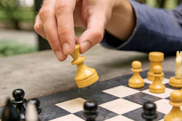 A man makes a move of a chess piece of a white queen on a board