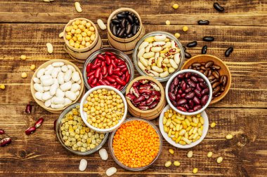 Kâselerdeki çeşitli kuru baklagiller sağlıklı bir yaşam tarzı için vazgeçilmez proteinler. Çeşitli fasulye çeşitleri. Ahşap masa arkaplanı, üst görünüm