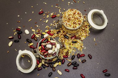 Cam kavanozlarda mısır gevreği ve fasulye karışımı. Sağlıklı bir yaşam tarzı için vazgeçilmez protein kaynakları. Siyah taş arkaplan, üst görünüm