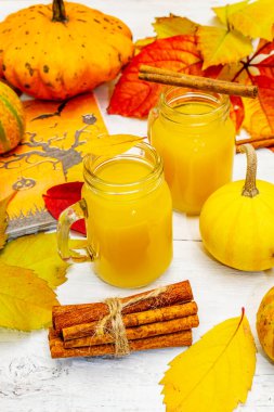 Alkolsüz portakal kokteyli. Bayramlık Cadılar Bayramı içeceği, dekoratif balkabakları, dökülen yapraklar ve tarçın çubukları. Beyaz tahta arka plan, kapat