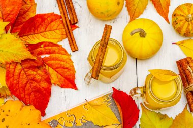 Alkolsüz portakal kokteyli. Bayramlık Cadılar Bayramı içeceği, dekoratif balkabakları, dökülen yapraklar ve tarçın çubukları. Beyaz tahta tahta arka plan, üst görünüm