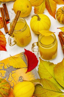 Alkolsüz portakal kokteyli. Bayramlık Cadılar Bayramı içeceği, dekoratif balkabakları, dökülen yapraklar ve tarçın çubukları. Beyaz tahta arka plan, kapat