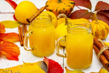 Alkolsüz portakal kokteyli. Bayramlık Cadılar Bayramı içeceği, dekoratif balkabakları, dökülen yapraklar ve tarçın çubukları. Beyaz tahta arka plan, kapat